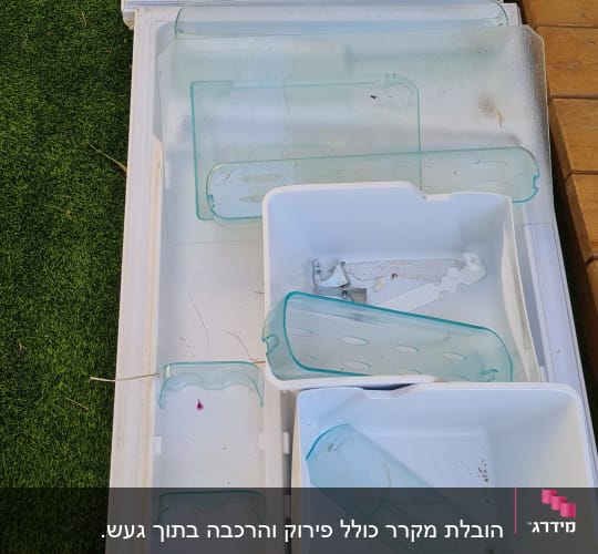 חלקי פלסטיק וזכוכית ממקרר מונחים על דשא